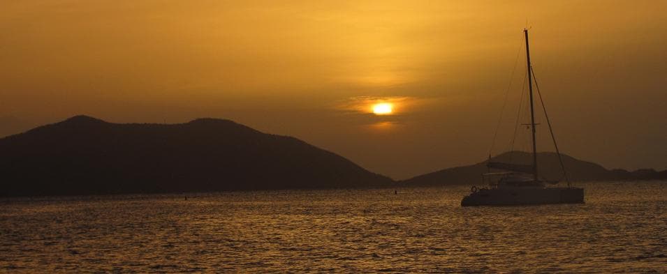 A catamaran at anchor against a tropical sunset